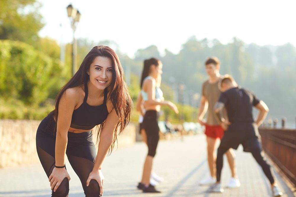 role of exercise in mental health - Young sporty girl smiles on the background of friends athletes in the park. Health. Healthy lifestyle.