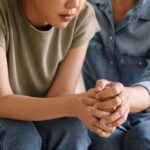 Close-up of two people sitting close together, one offering comfort and support with a hand on the other's shoulder