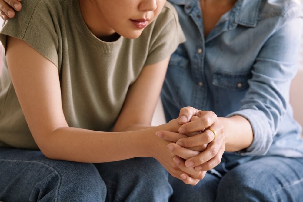 Close-up of two people sitting close together, one offering comfort and support with a hand on the other's shoulder