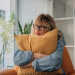 woman sitting on the couch hugging a pillow, looking anxious or stressed out