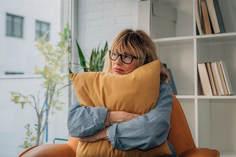 woman sitting on the couch hugging a pillow, looking anxious or stressed out