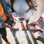 Group of teens standing close together, using smartphones—capturing the influence and prevalence of social media in youth culture.