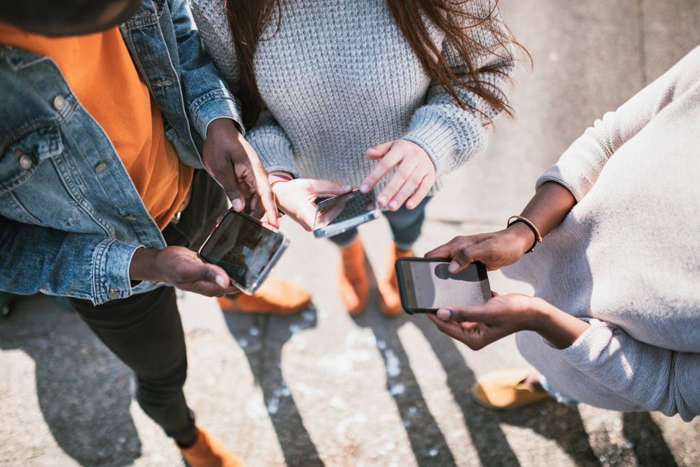 Group of teens standing close together, using smartphones—capturing the influence and prevalence of social media in youth culture.