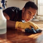 Man wearing gloves intently scrubbing a wooden surface with a cloth, symbolizing repetitive cleaning behavior.