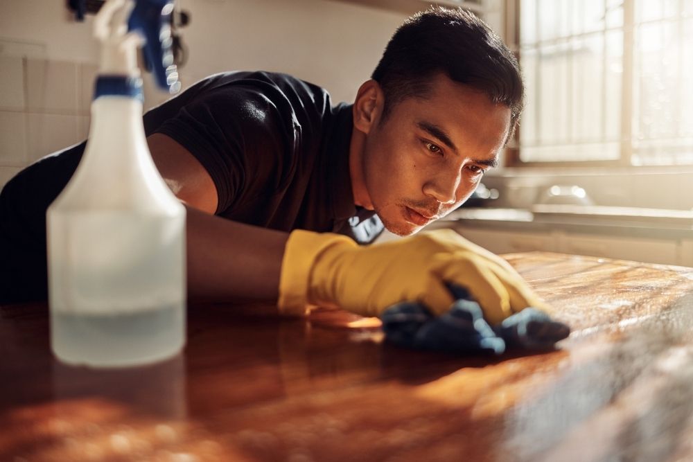 Man wearing gloves intently scrubbing a wooden surface with a cloth, symbolizing repetitive cleaning behavior.