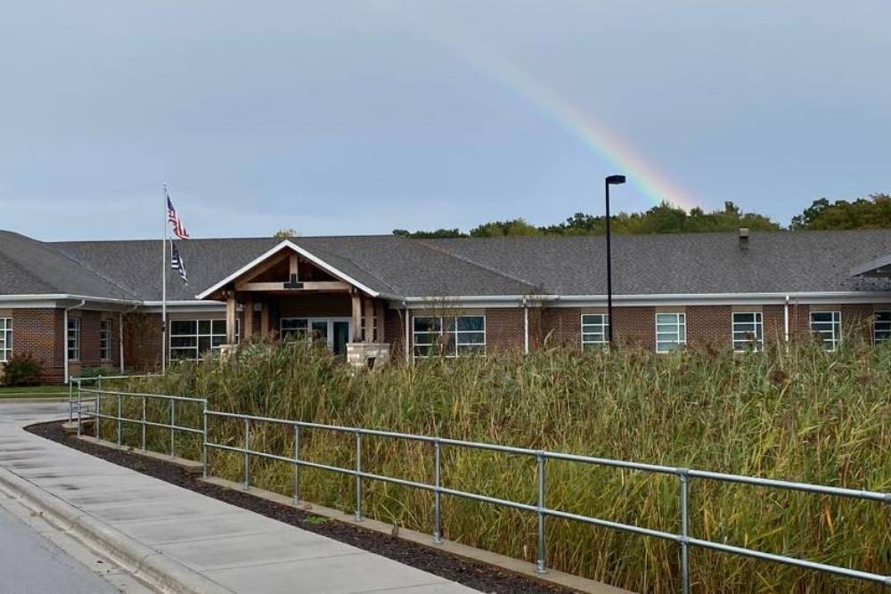 Exterior view of Willow Creek Behavioral Health, a brick building with an American flag, surrounded by tall grasses and a rainbow in the sky.